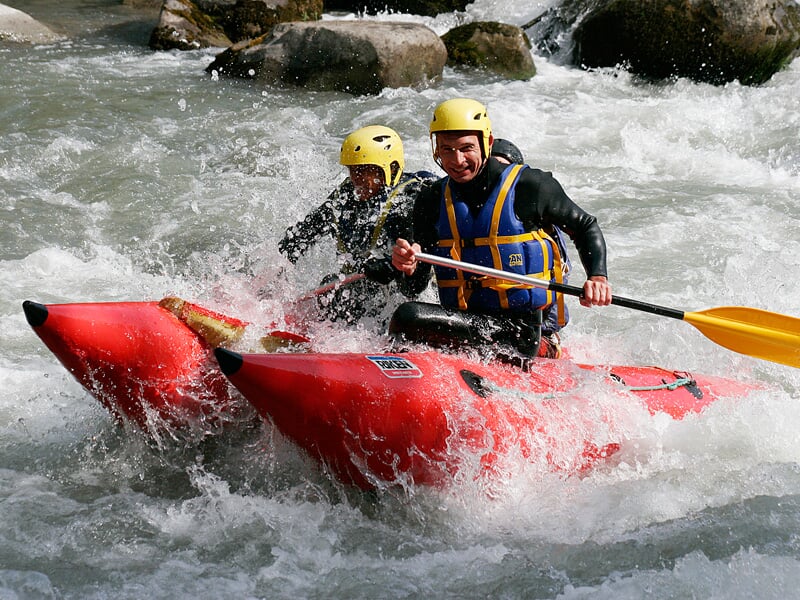 Deux hommes en raft rouge pagaient dans une rivière avec des rapides et éclaboussures d'eau vive.