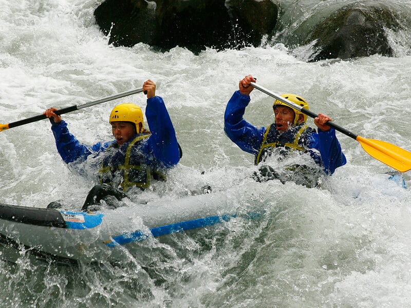 Groupe de personnes en canoë-raft bleu et jaune pagaient dans une rivière avec des rapides.