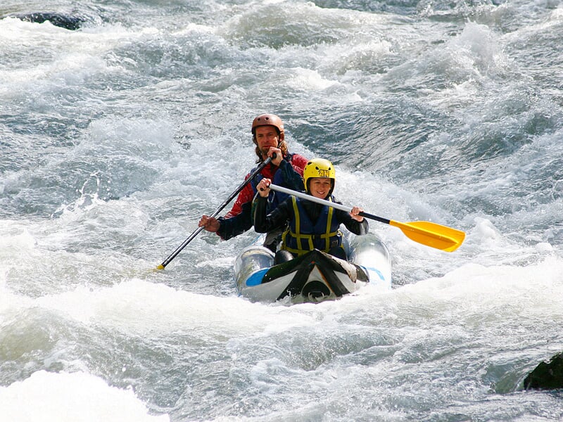 Quatre personnes en canoë-raft bleu et jaune pagaient dans une rivière avec des rochers et rapides.