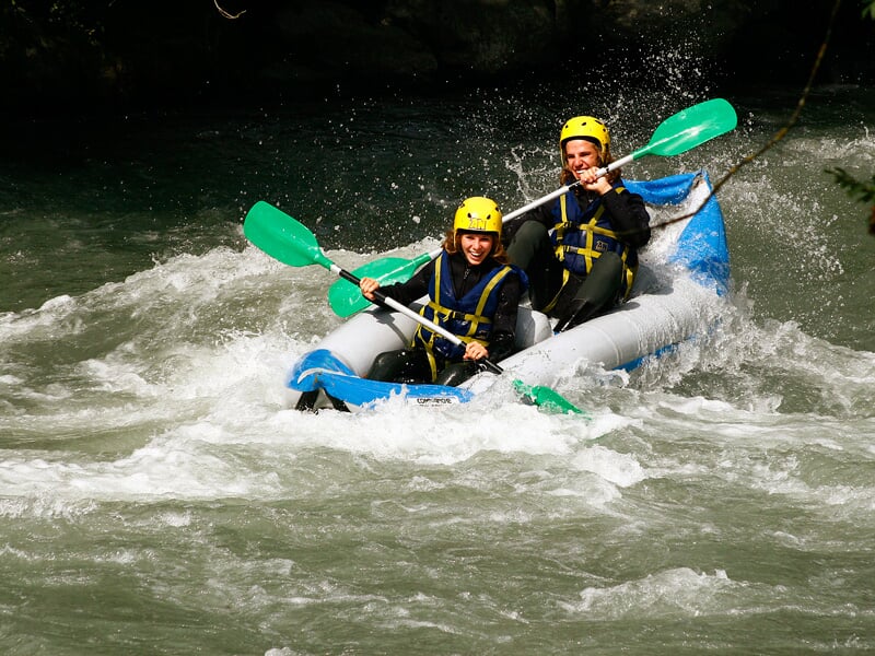 Deux hommes en canoë-raft rouge pagaient vigoureusement dans une rivière avec des rapides.