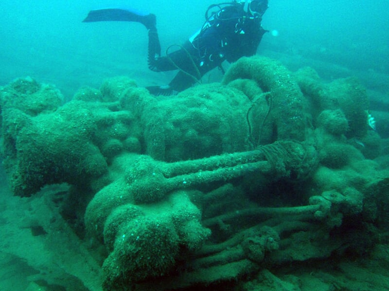 Plongeur explorant une épave sous-marine recouverte d'algues et de coraux dans une eau claire.