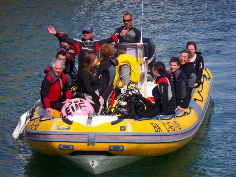 Groupe de plongeurs en combinaison sur un bateau pneumatique jaune en mer, prêts pour la plongée.