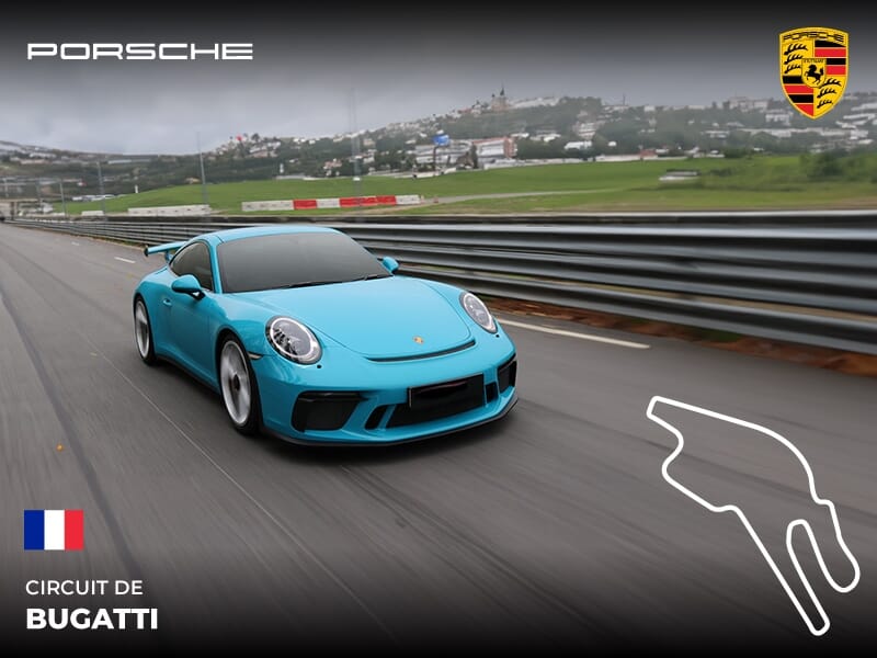 Voiture de sport Porsche bleue roulant rapidement sur le circuit Bugatti au Mans avec paysage urbain en arrière-plan.